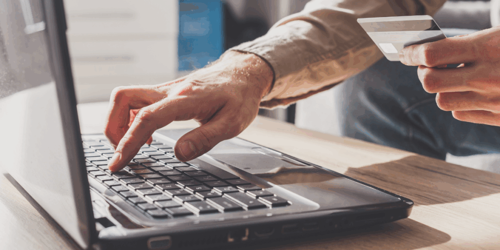 Mano che digita su un laptop mentre tiene una carta di credito, simbolo di pagamento online e transazioni digitali.
